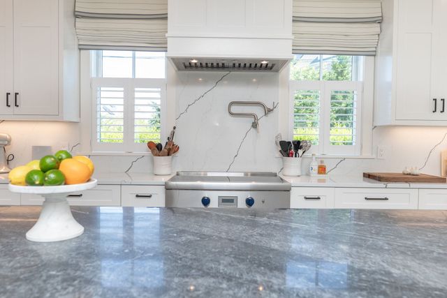 Bright white kitchen with blue marble countertop, stove, sink, and fruit bowl by the window