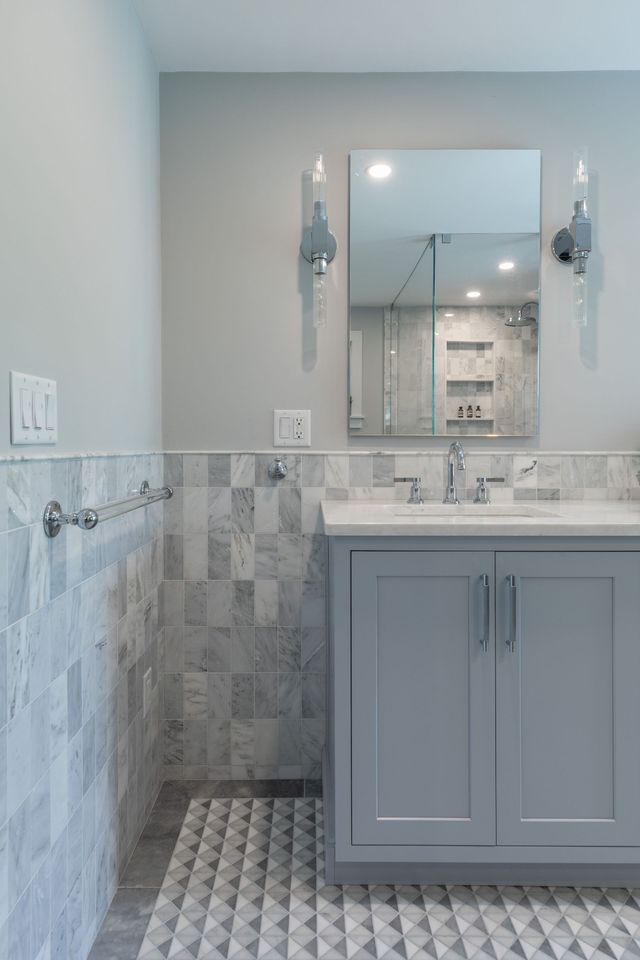 Small bathroom vanity with gray cabinet, marble countertop, mirror, and tiled walls and floor.