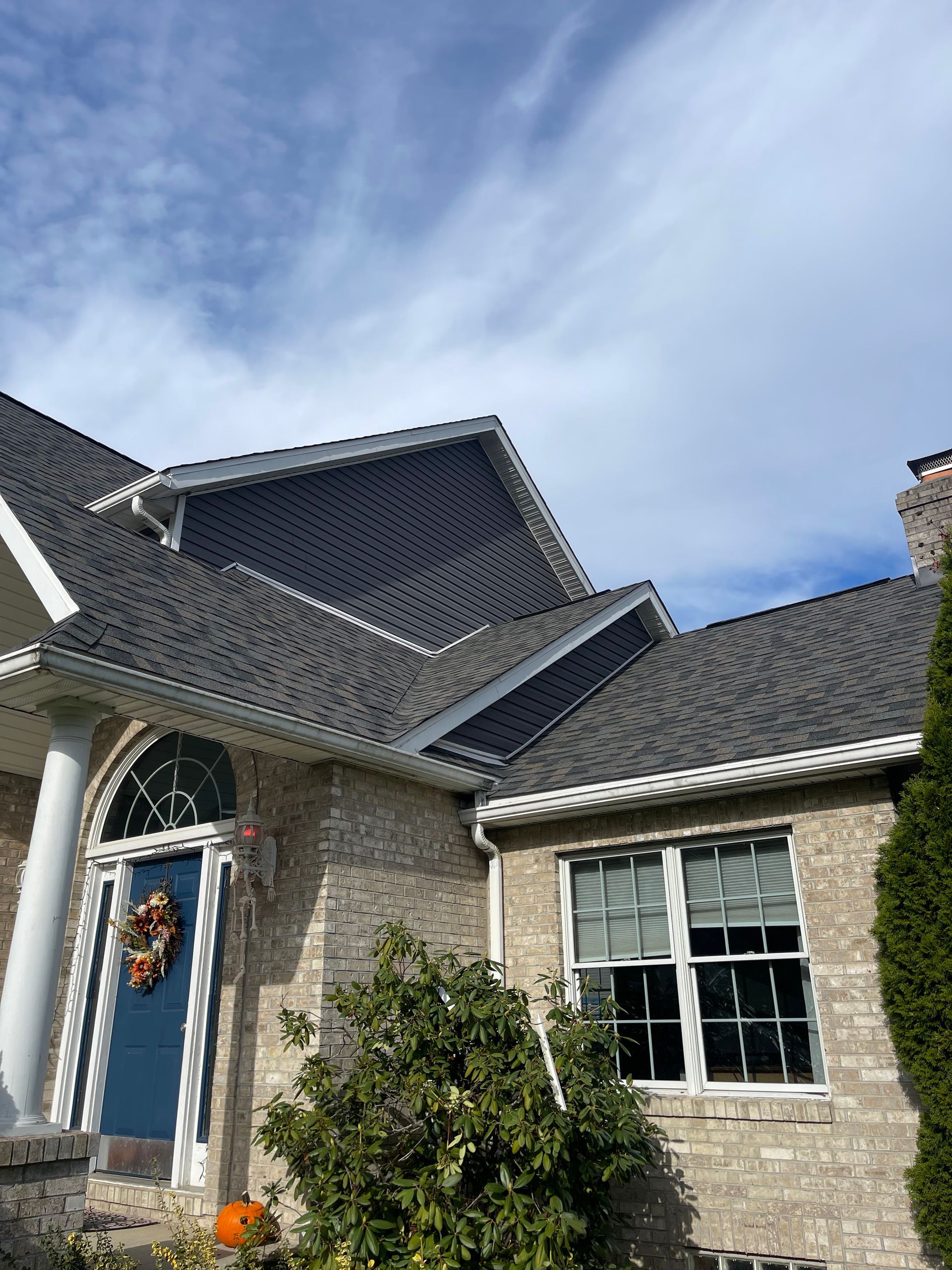 Brick house with dark roof and white trim under a cloudy sky.