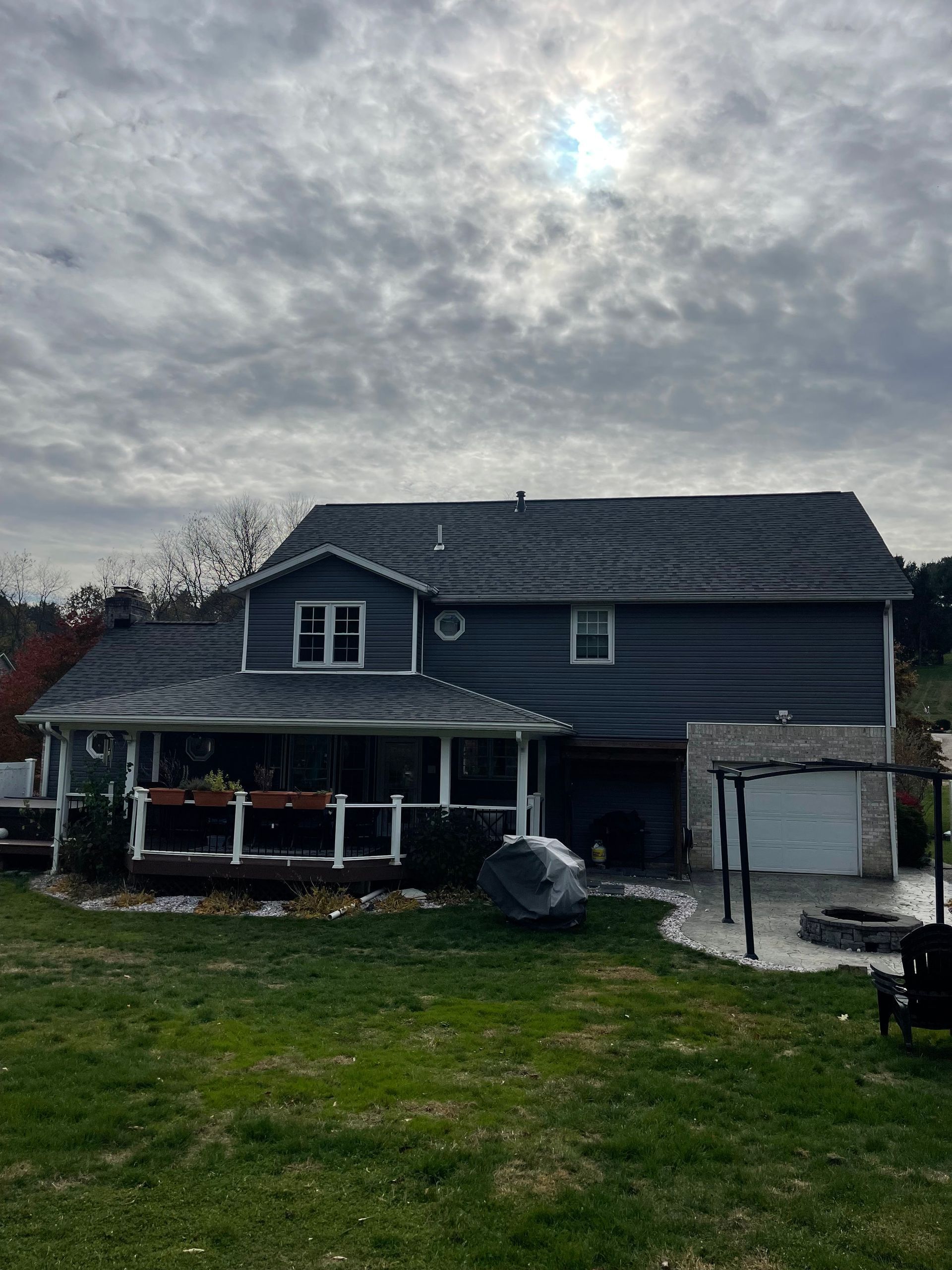 Blue house with porch and gray roof under a cloudy sky, back yard with lawn and patio.