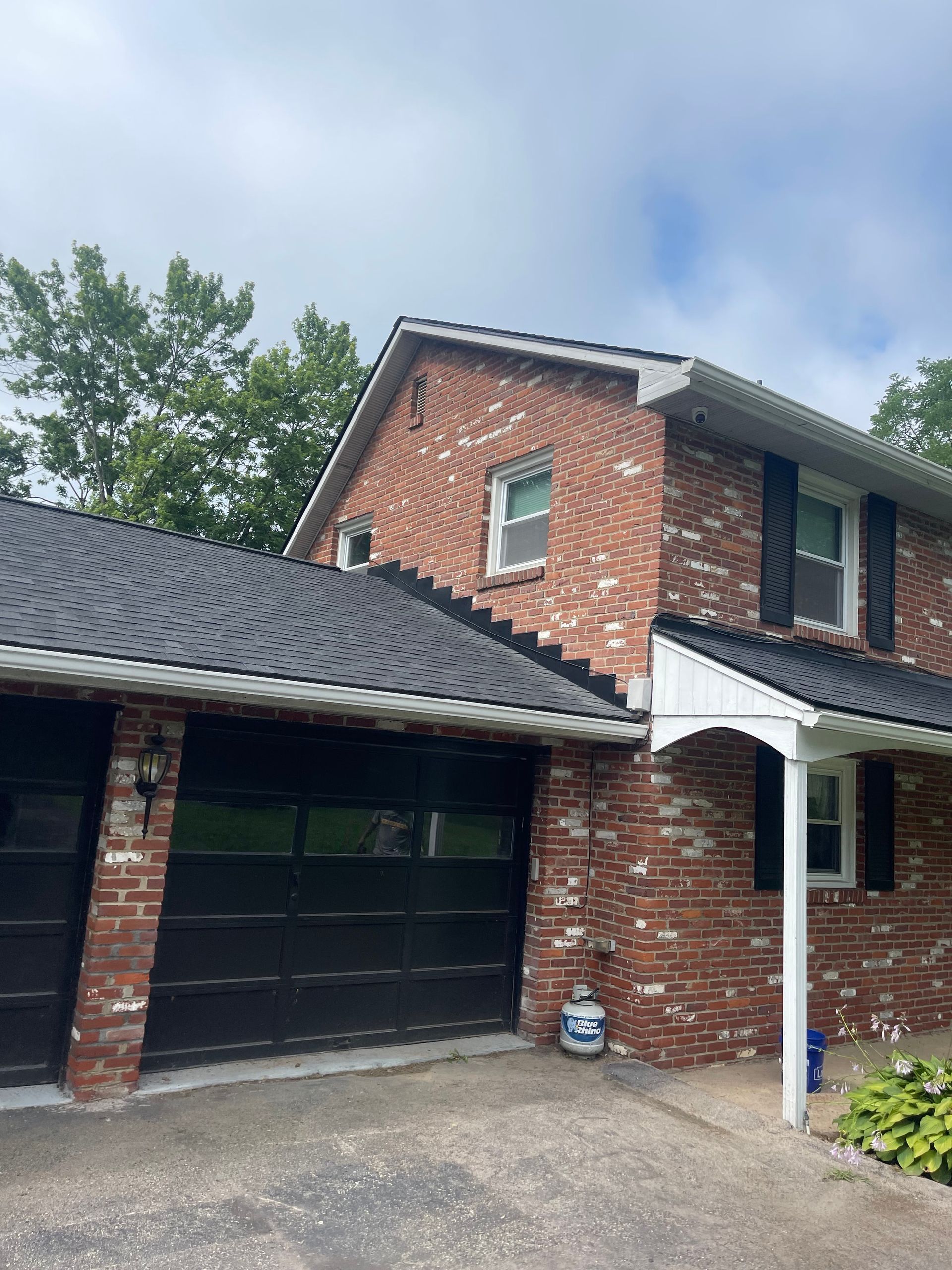 Brick house with black garage doors, shutters, and dark roof under a cloudy sky.