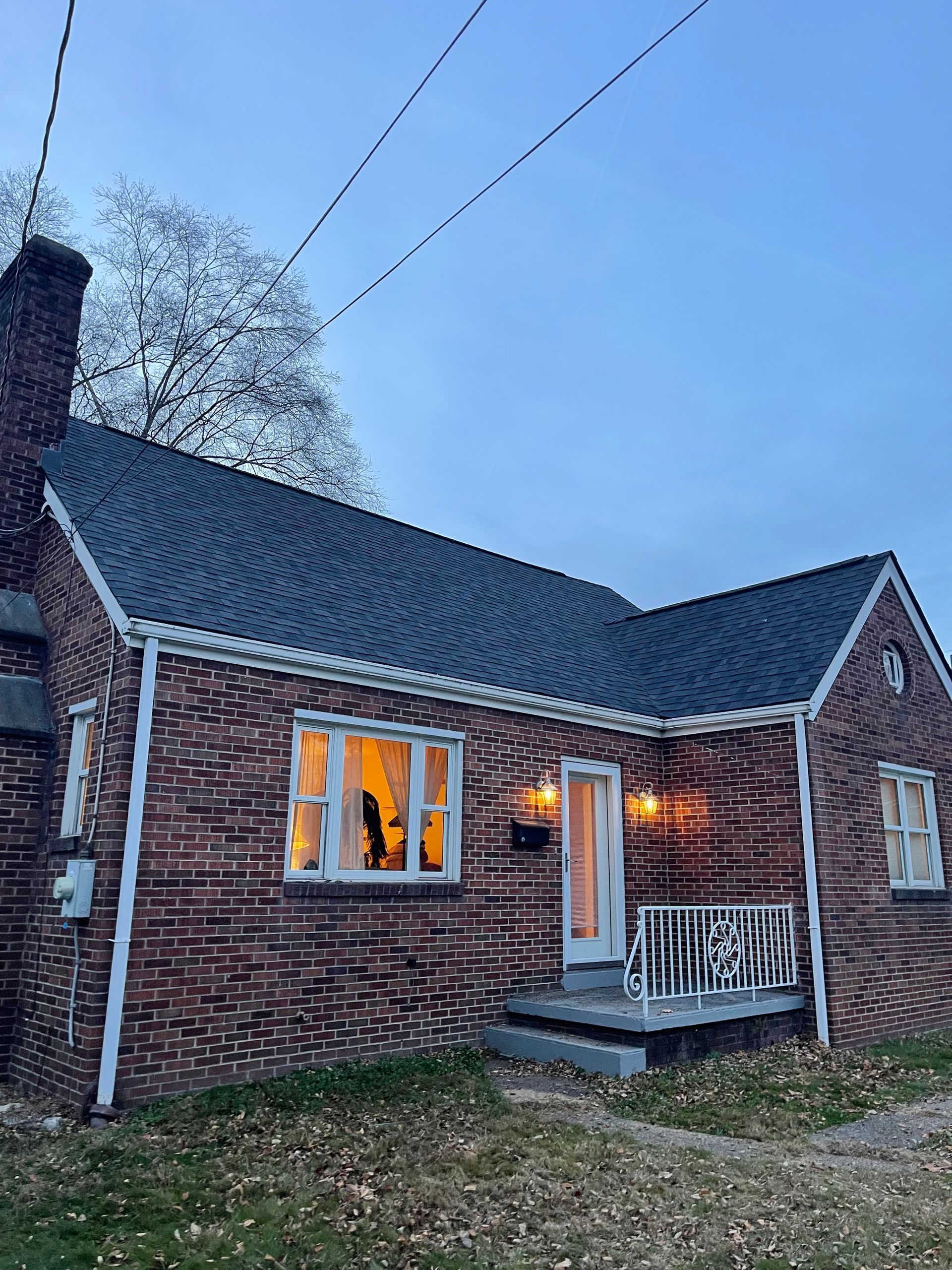 Brick house with lit windows and open doorway under an evening sky.