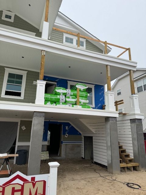 Two-story house under construction with a porch and stacked insulation. Blue wrap on walls.