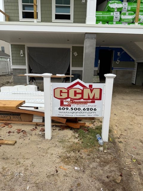 Construction site with a GCM Construction sign. Building with green siding, white trim and visible construction materials.
