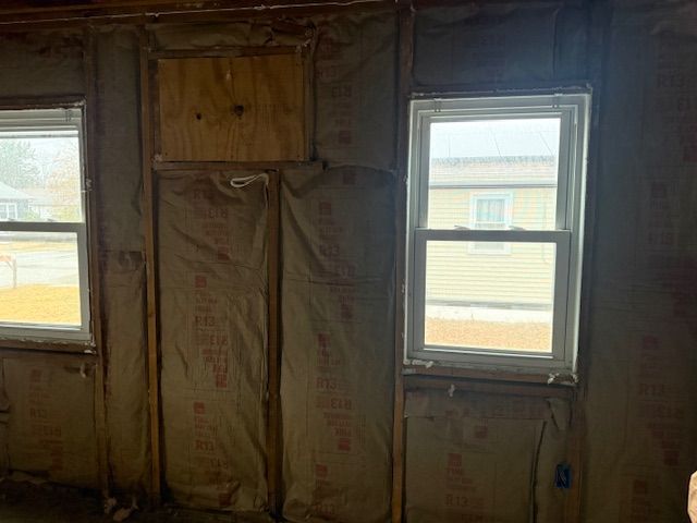 Interior view of a room with insulation, two windows, and plywood covering a section of the wall.