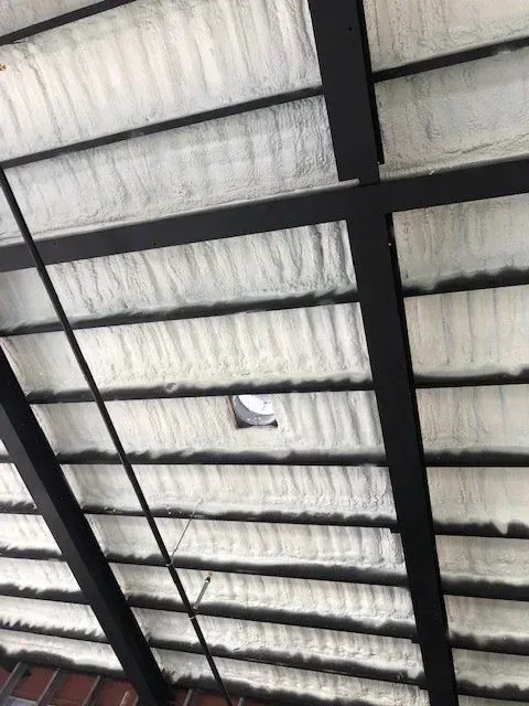 Black metal beams supporting a white, textured roof with a small opening.