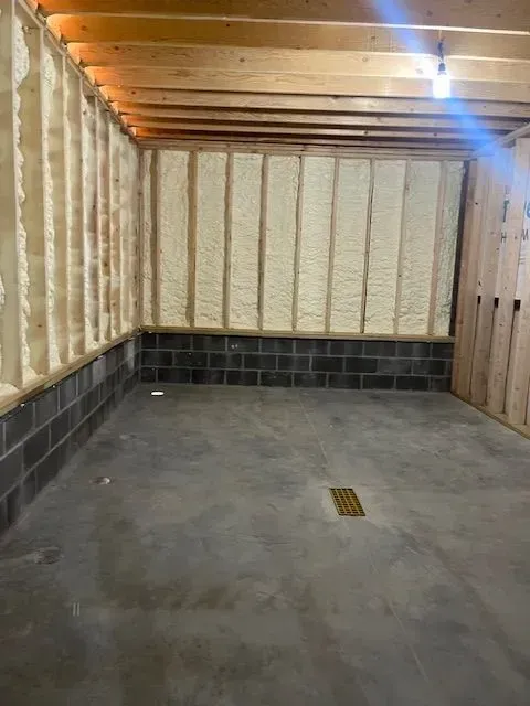 Interior of a room with exposed wooden studs, spray foam insulation, gray concrete floor, and brick base.