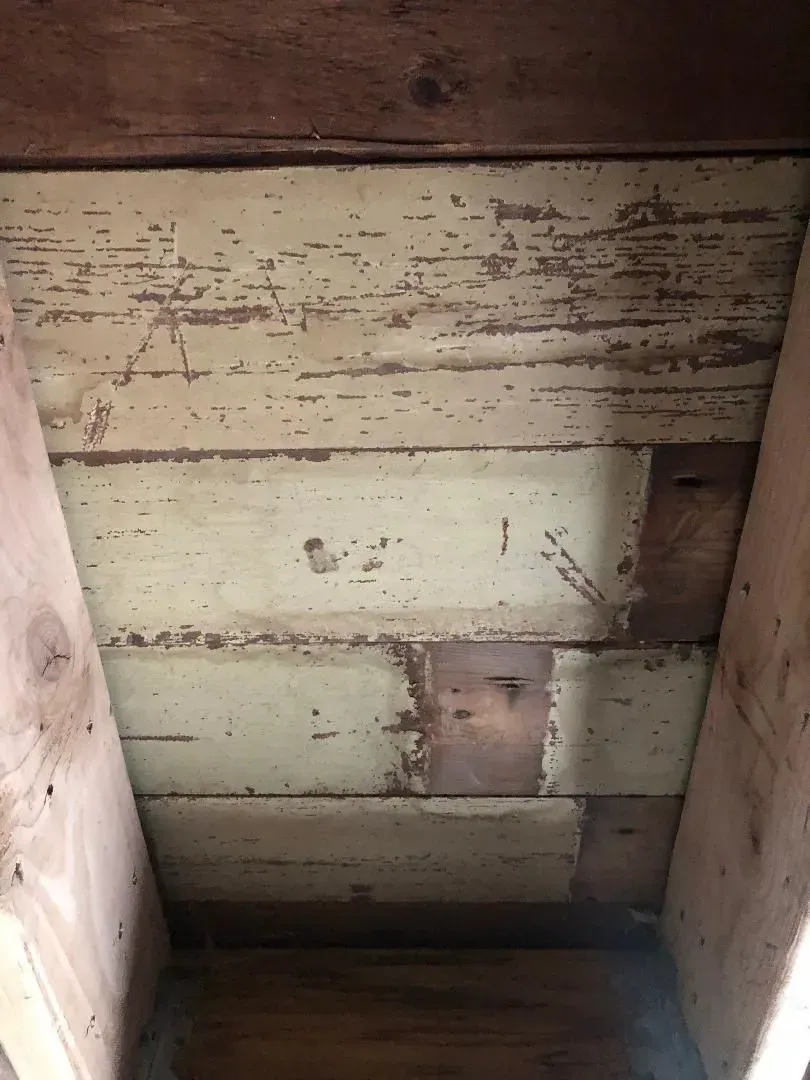 Wooden planks forming a ceiling, painted in faded yellow, between wooden beams.