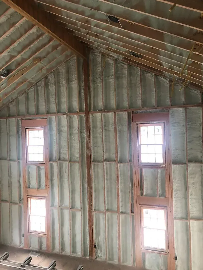 Interior view of a building with spray foam insulation visible on walls and ceiling, framing windows.