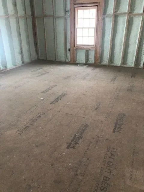 Interior room with spray foam insulation on walls, window, and brown flooring.