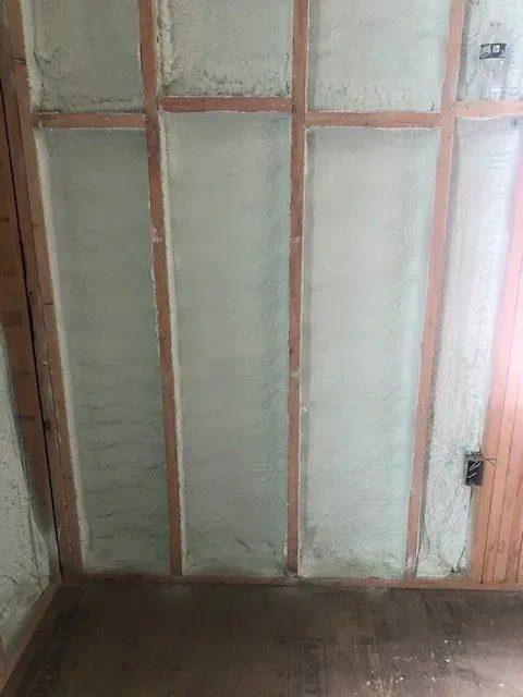 Wooden wall frames filled with light green spray foam insulation.