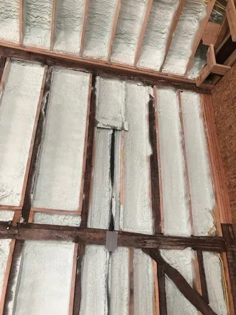 Interior wall with exposed wooden beams and spray foam insulation in a construction setting.