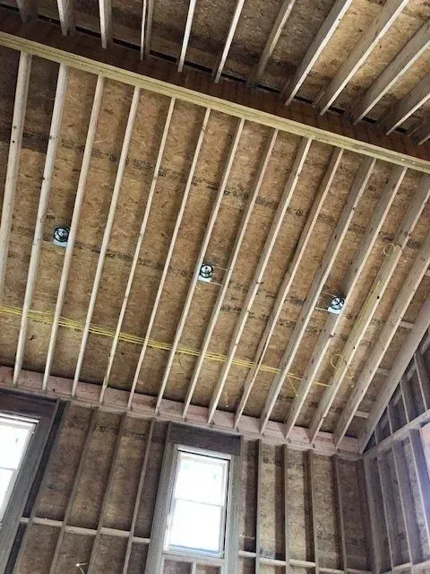 Wooden roof framing with electrical boxes and wiring; windows visible in the wall.