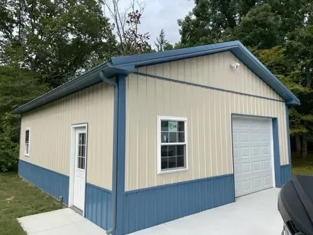Beige and blue metal garage with a white door, window, and garage door, set outdoors.