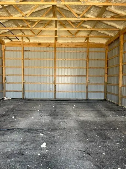 Interior of a large empty barn with wooden beams and metal siding. Dark flooring.