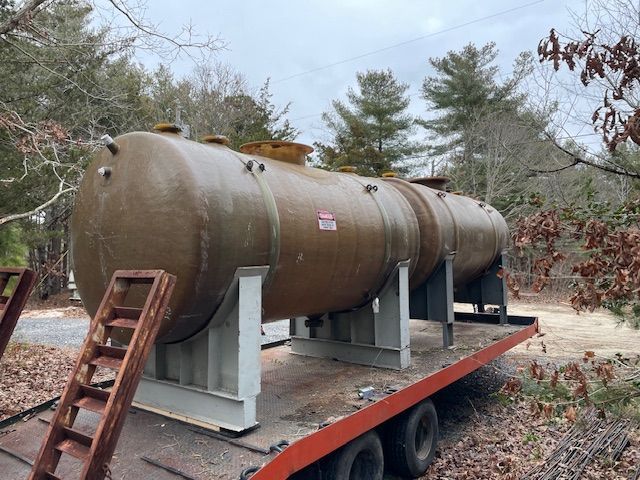 Large brown cylindrical tank on a flatbed trailer, supported by metal beams, outdoors.