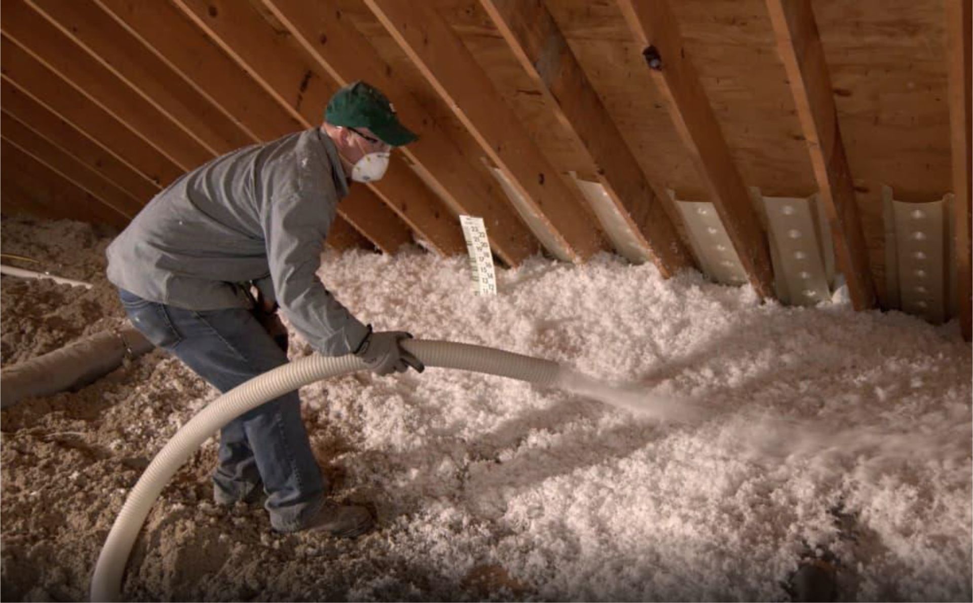 Worker blowing insulation into an attic with a hose under exposed wooden rafters