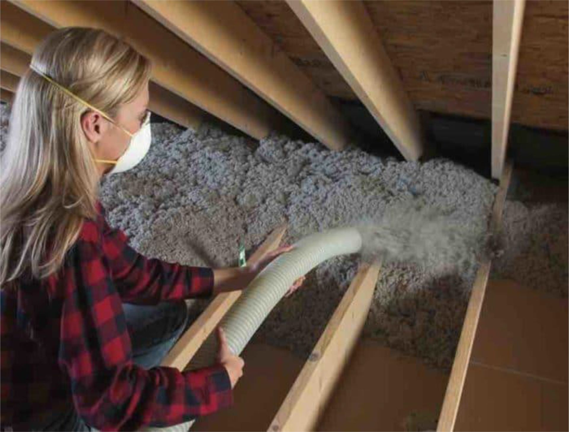 Person in a mask blowing insulation into an attic with a hose