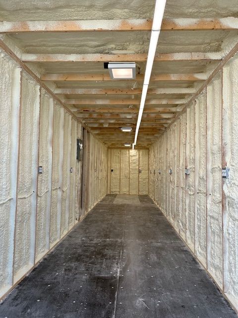 Interior of a bare spray-foam insulated storage room with concrete floor and ceiling light.