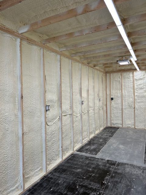 Spray-foam insulated unfinished basement with exposed wood joists and concrete floor.