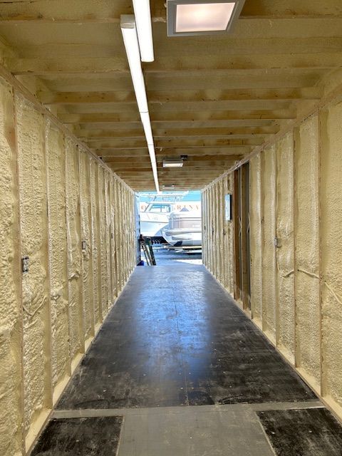 Long insulated hallway with a concrete floor and fluorescent lights, opening to a brighter outdoor area.