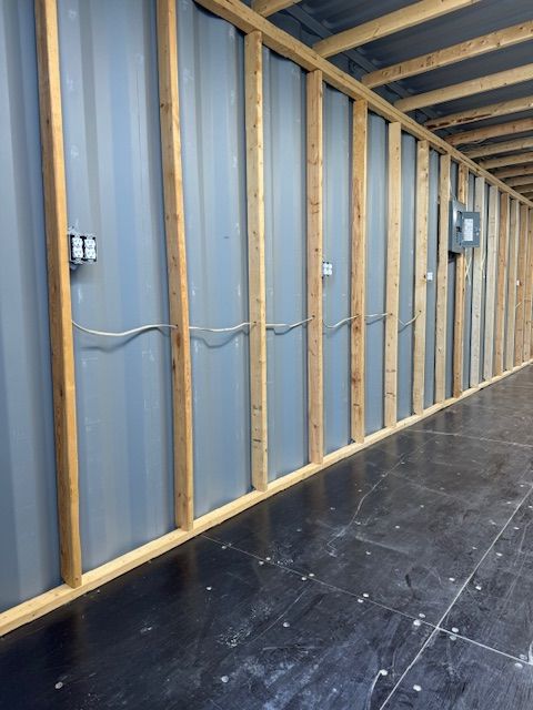 Empty interior wall framing with blue insulation, exposed studs, and black floor decking