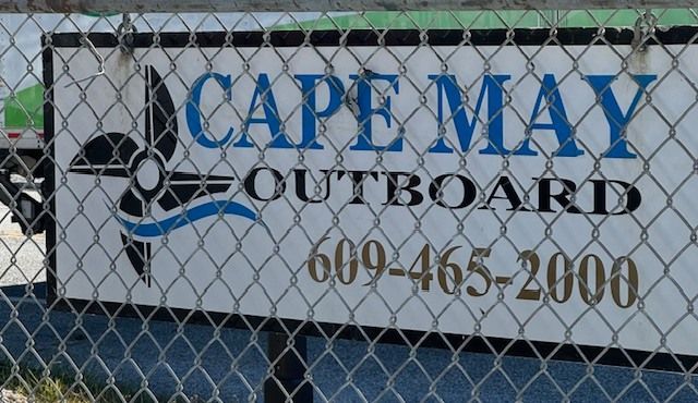 Cape May Outboard sign on a chain-link fence with blue and black lettering and phone number 609-465-2000
