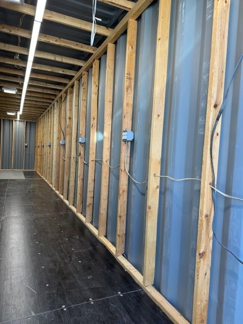 Unfinished interior wall framing with exposed wood studs, blue sheathing, and a concrete floor hallway