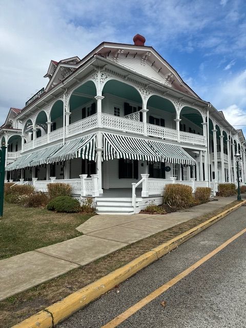 White Victorian building with green and white awnings and porch, set on a sidewalk.