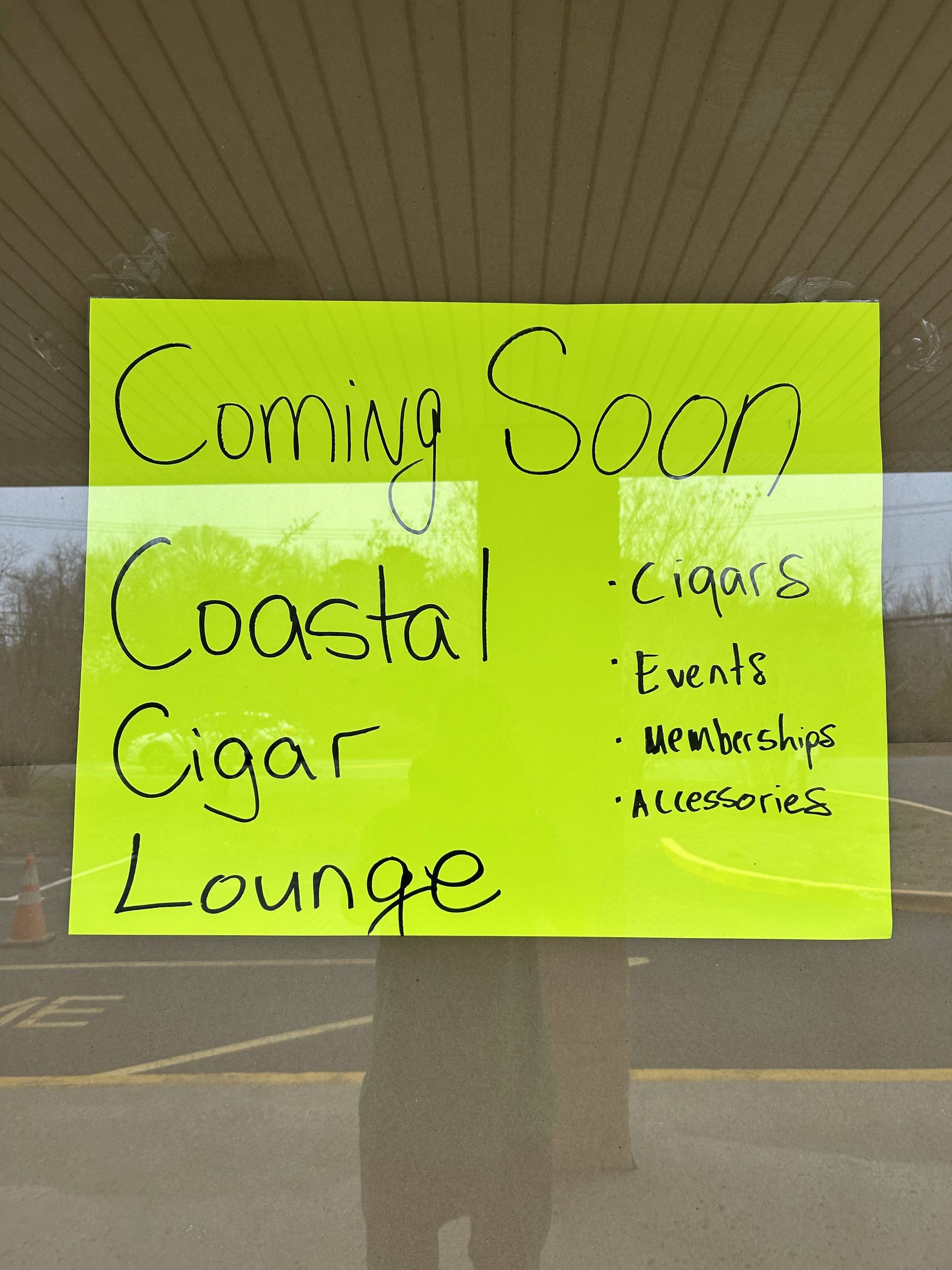 Neon yellow Coming Soon sign for Coastal Cigar Lounge on a storefront window.