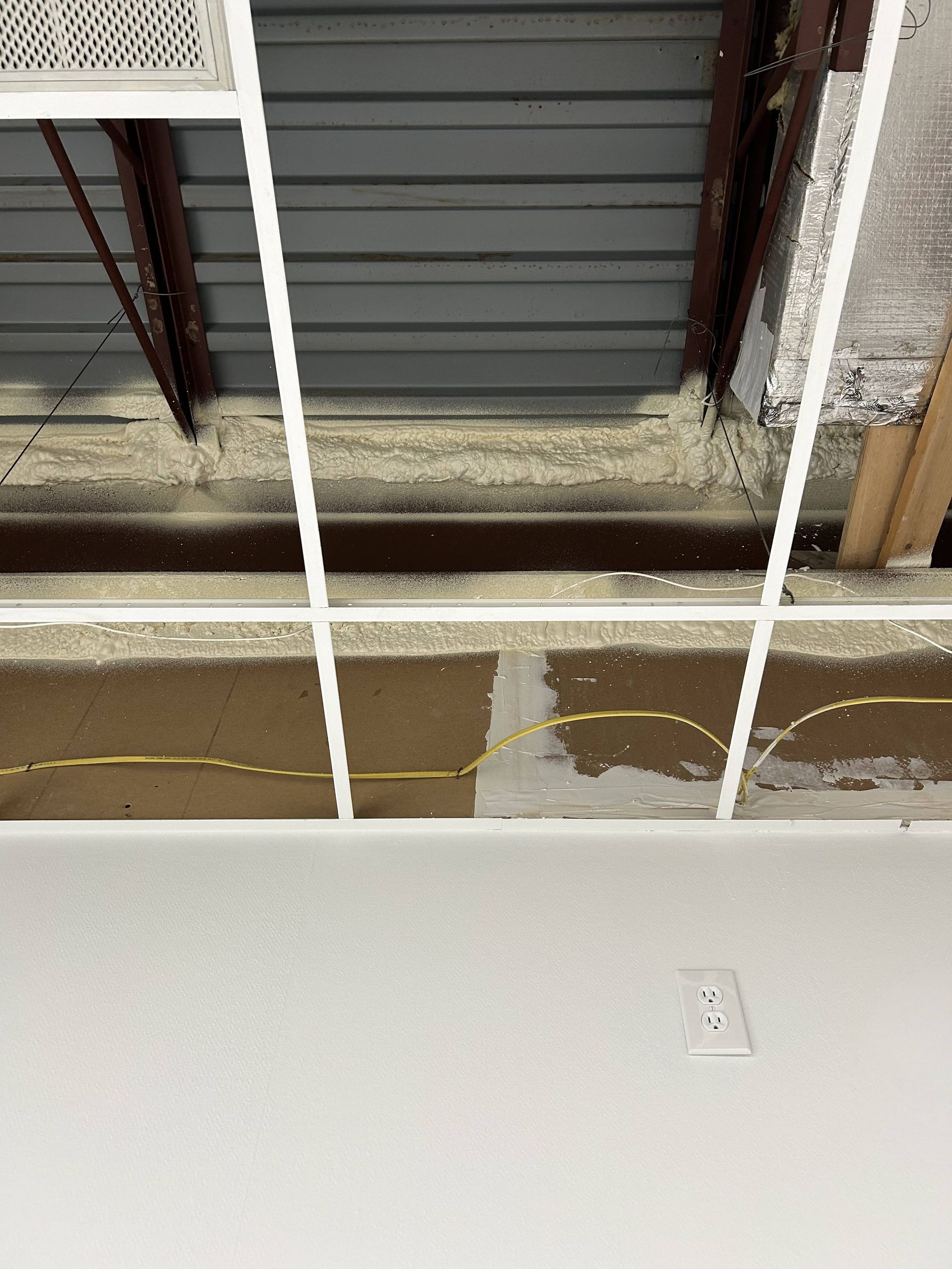 Damaged ceiling with exposed beams, water stain, and cracked plaster above a white wall.