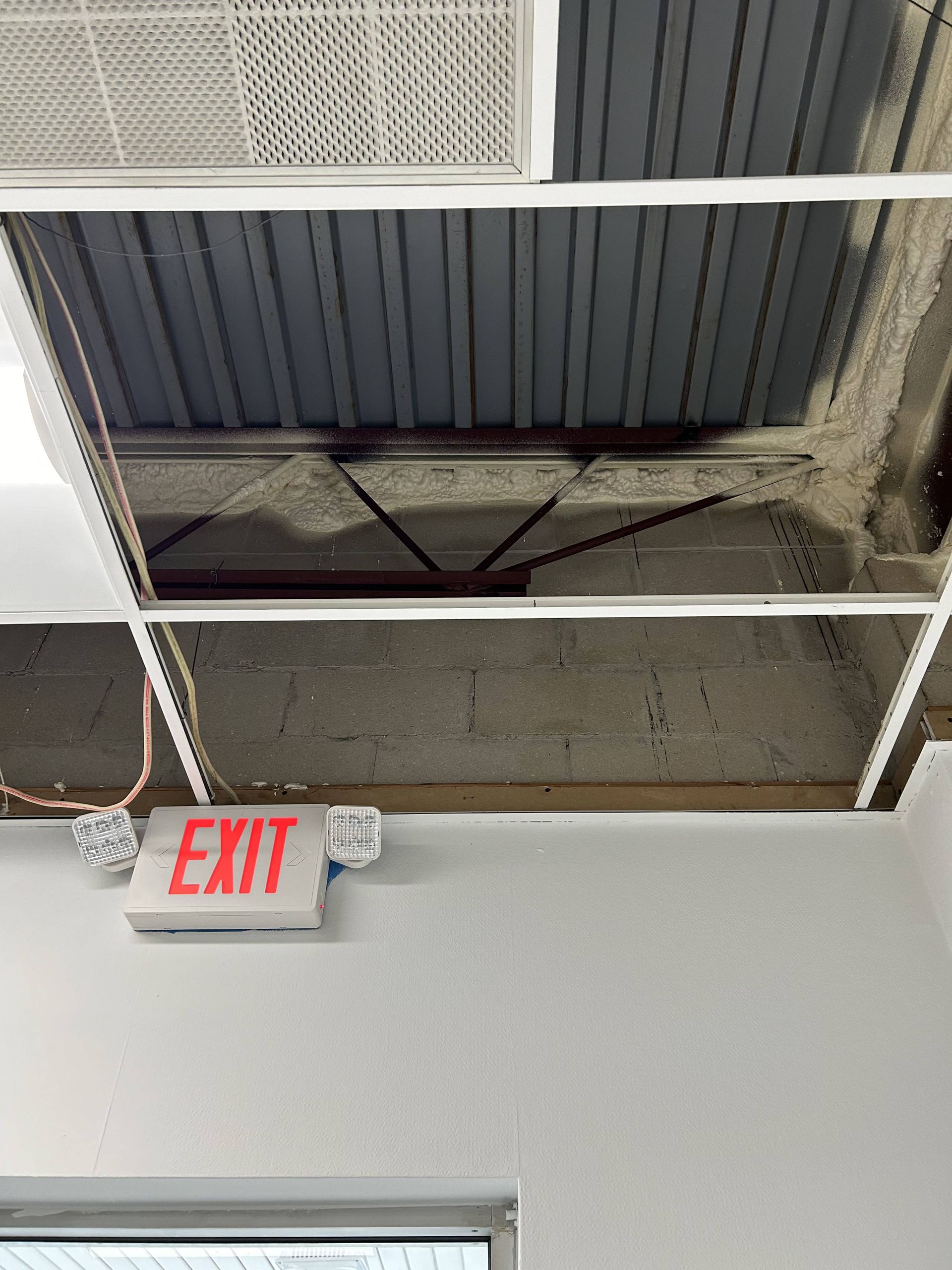 Ceiling with exposed ductwork and fluorescent lights above a red EXIT sign in a hallway