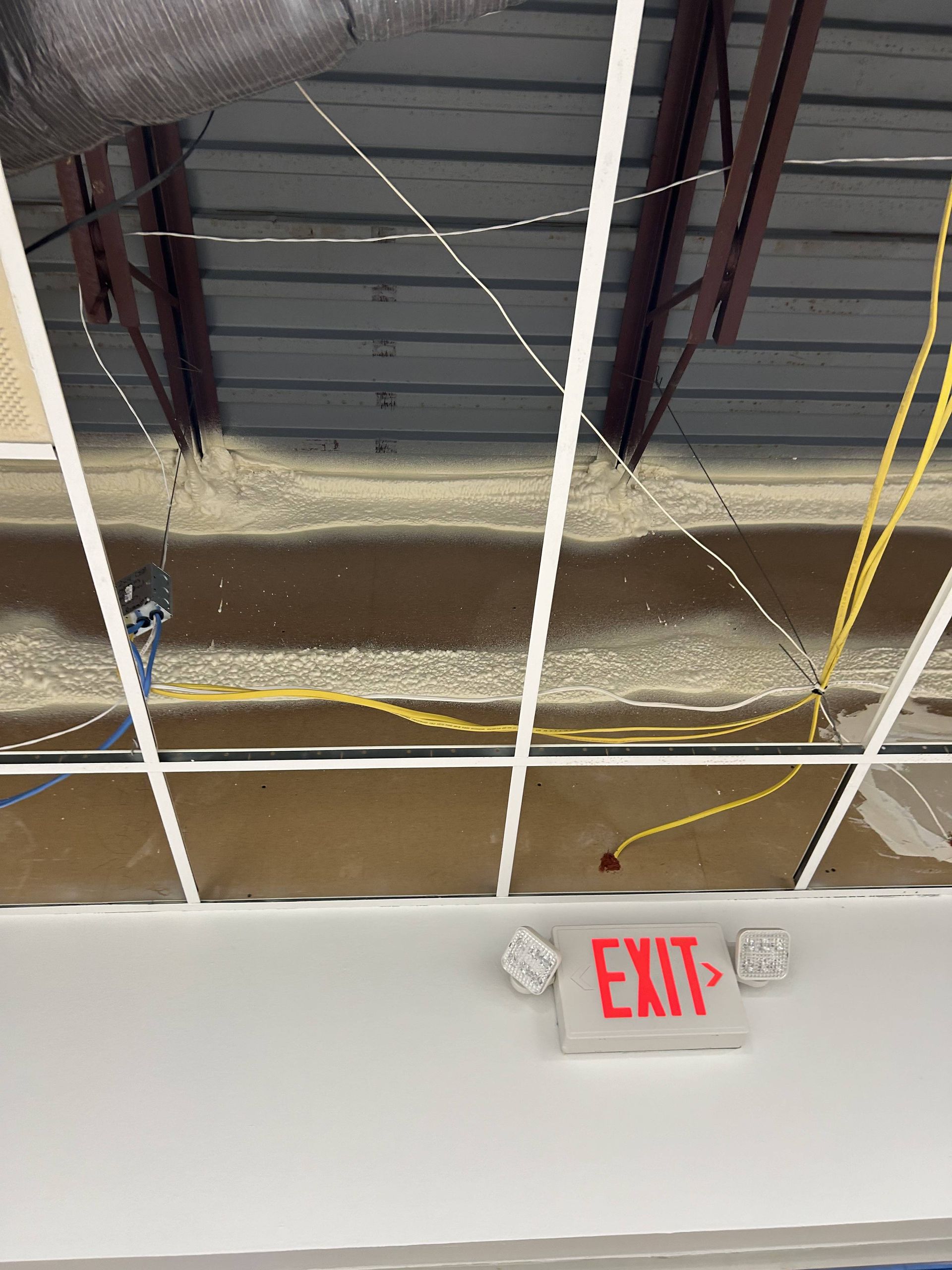 Ceiling with exposed wires and insulation above a wall-mounted red EXIT sign