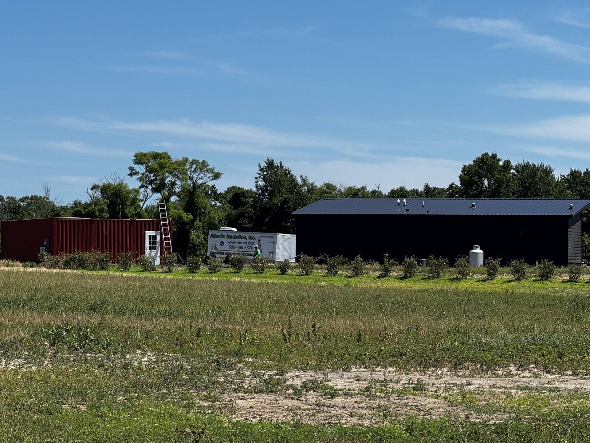 Open field with a black building, white truck, and red container under a blue sky
