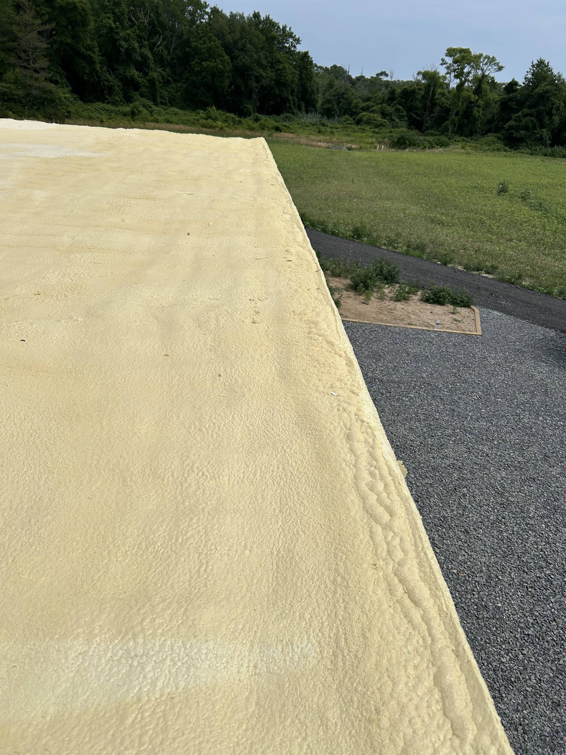 Yellow gravel ramp beside a gravel path and grassy field with trees in the background