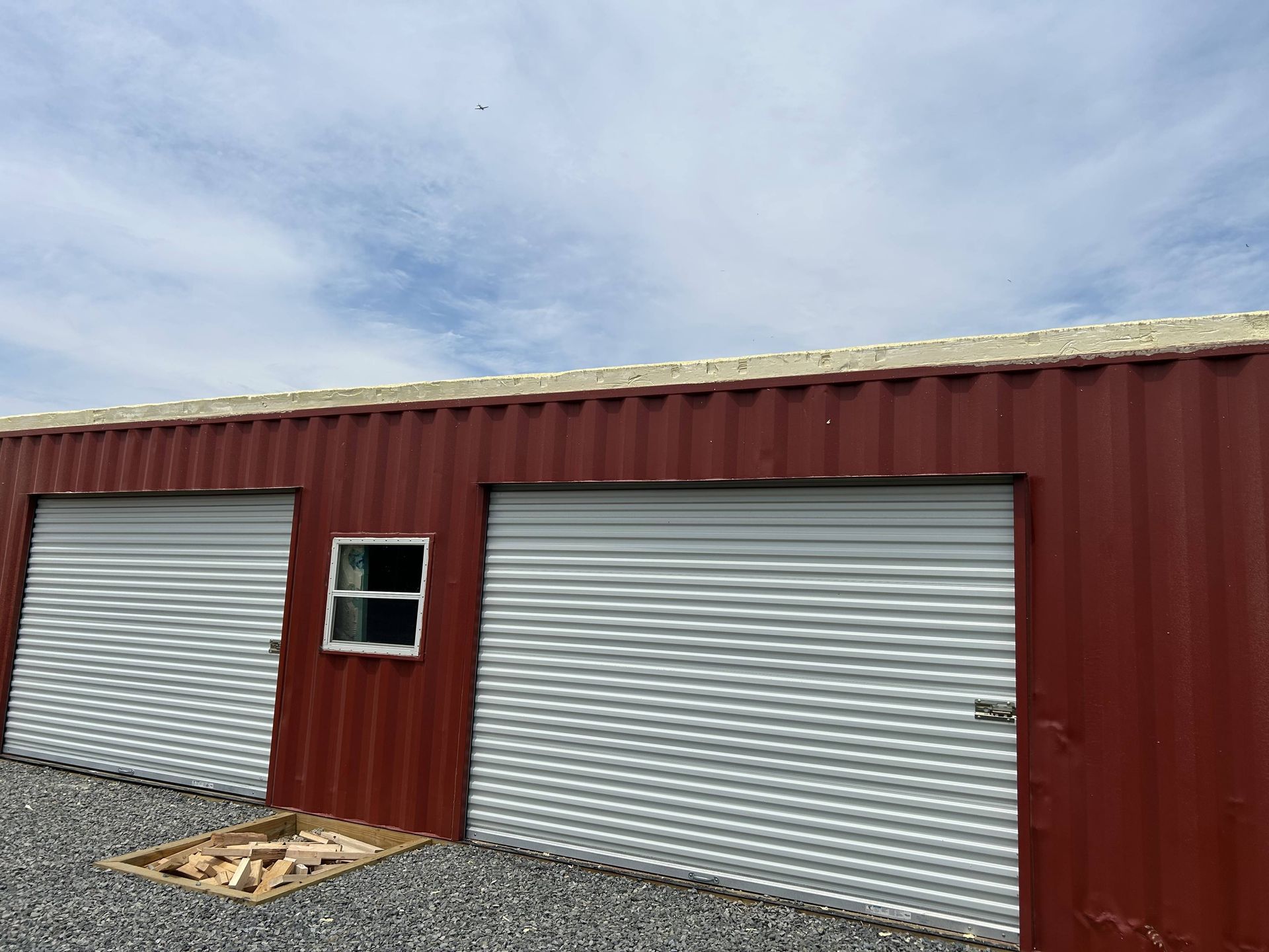 Red metal building with two closed white roll-up doors and a small window under a cloudy sky.