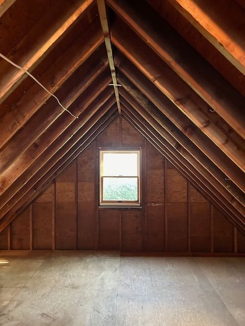 Empty attic with wooden beams, window in the center. Sunlight streams through.