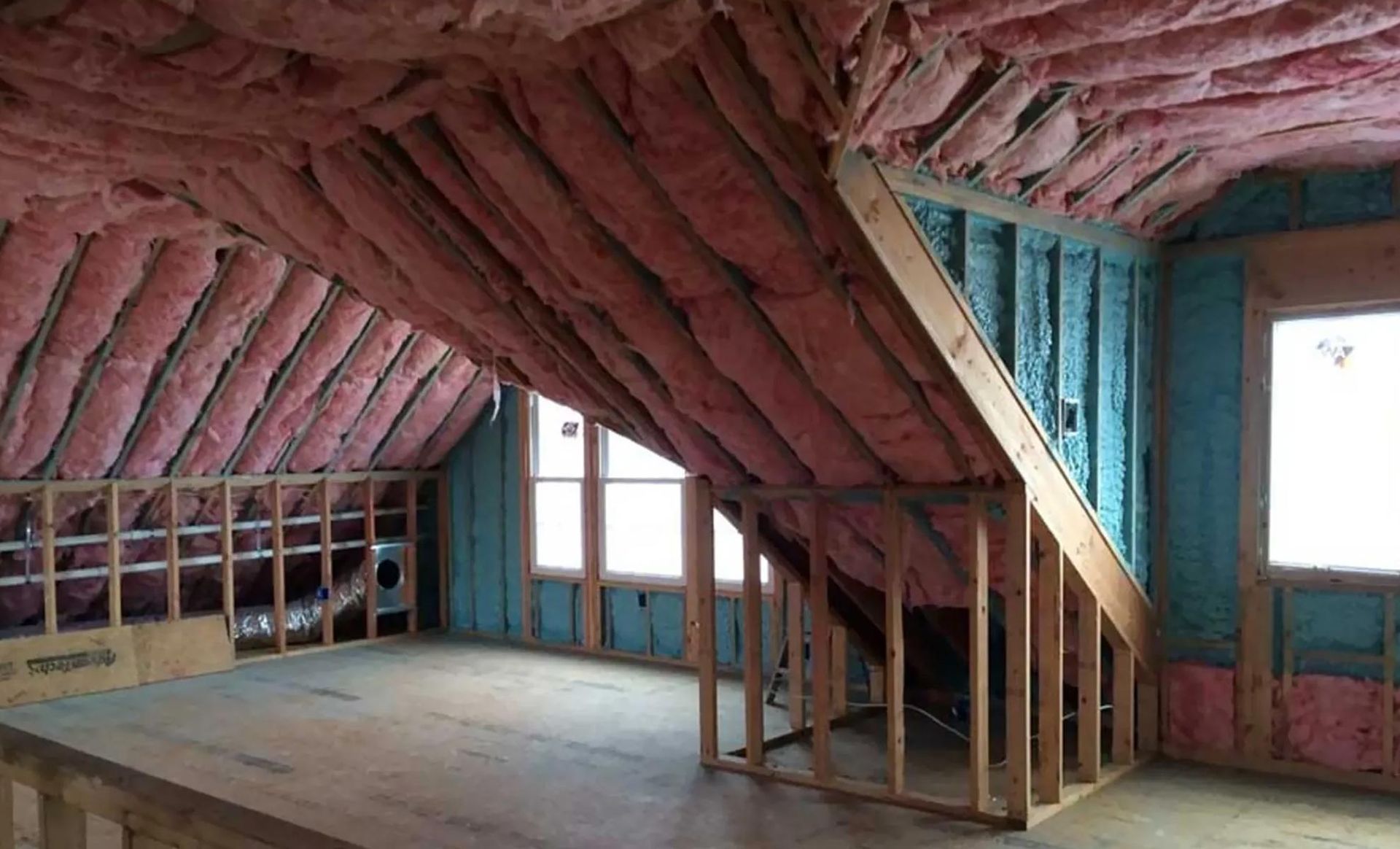 Interior of a room under construction, with pink insulation in the sloped ceiling and blue insulation on the walls.