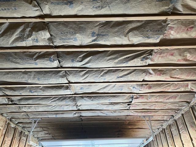 Insulation installed between wooden beams in a ceiling, viewed from below.