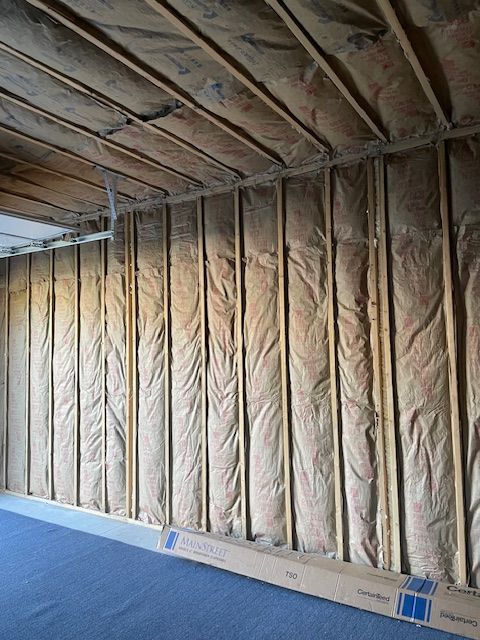Interior wall with insulation between wooden studs, awaiting drywall.