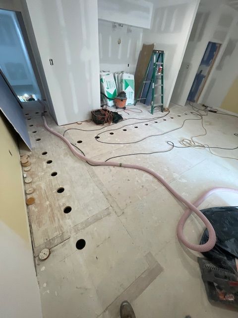 Room under construction with exposed flooring, tools, and materials; a large pink hose runs across the floor.