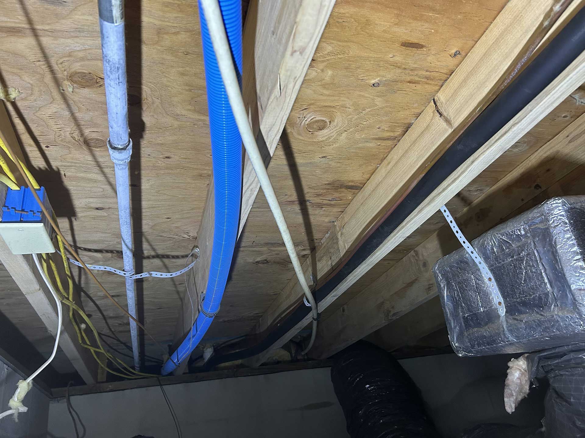 Exposed ceiling joists with various cables, a blue corrugated conduit, a white pipe, and a suspended HVAC duct.