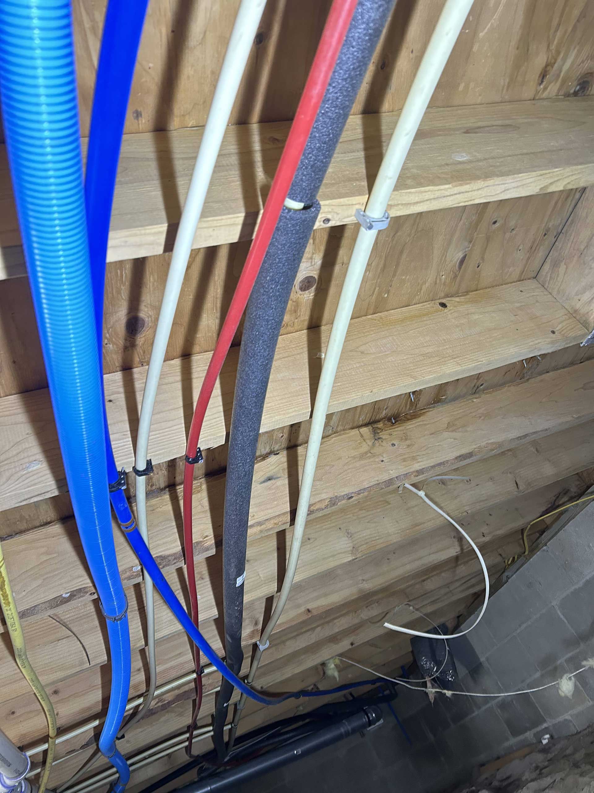 A blue flexible conduit and several PEX water lines—white, red, and insulated black—run vertically against wooden studs.