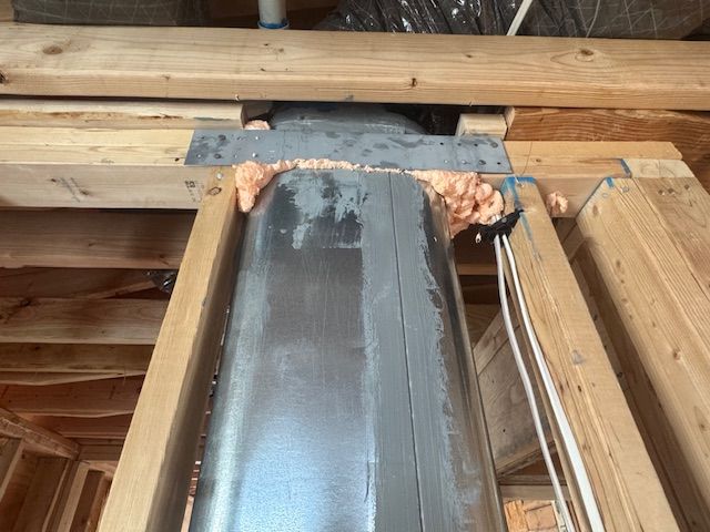Metal ductwork passing through wooden supports, sealed with foam.
