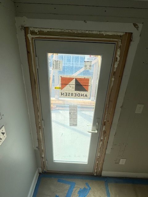 White Andersen exterior door framed by wood trim in a room with light gray walls.