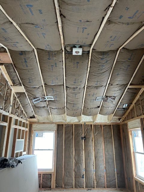 Interior view of a room under construction with exposed wooden beams, insulation, and electrical fixtures.