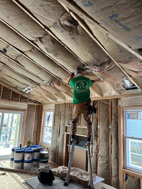 Worker on stilts installing insulation in a new house. Interior view, beige walls, windows.