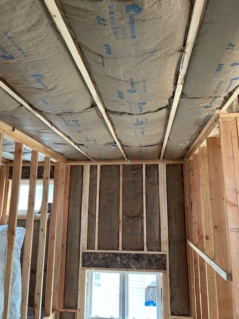 Interior view of a building under construction, showing wooden framing and insulation in the walls and ceiling.