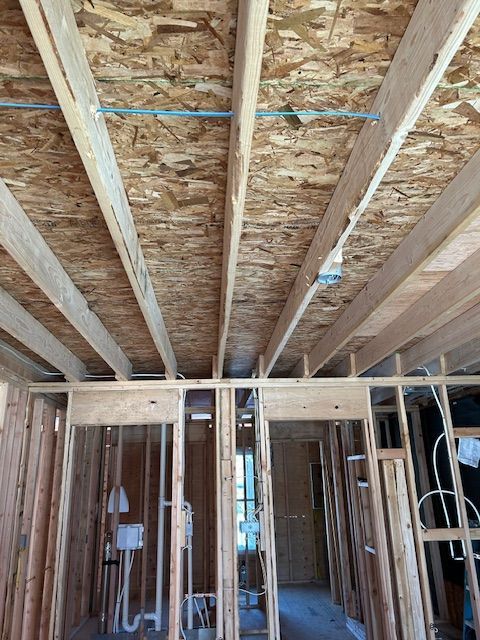 Interior construction with exposed wooden beams, studs, and OSB ceiling. Plumbing and wiring visible.