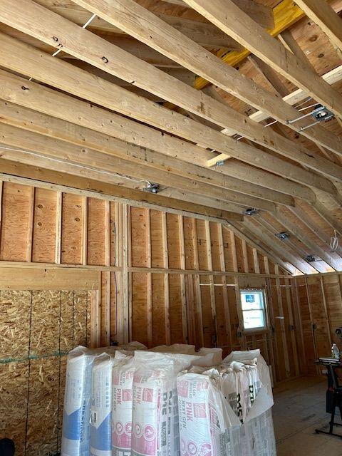 Interior of a building under construction, showing wooden framing, insulation, and bags of insulation.